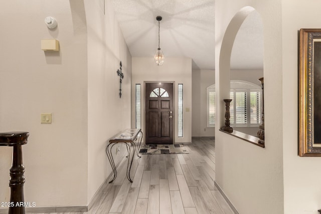 foyer entrance featuring arched walkways, baseboards, and wood finished floors