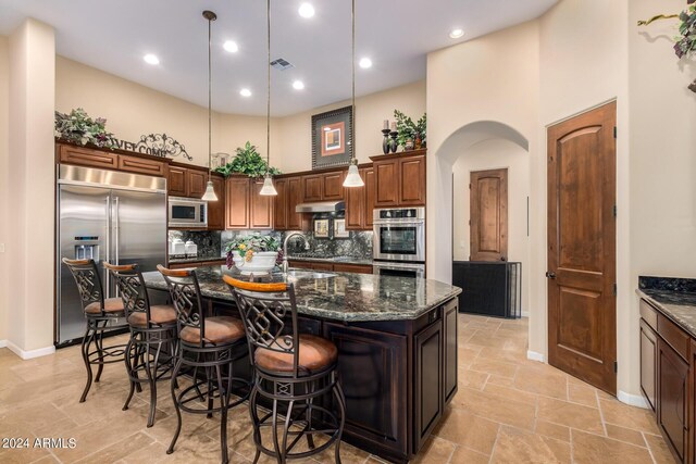 kitchen featuring built in appliances, decorative light fixtures, sink, and a large island