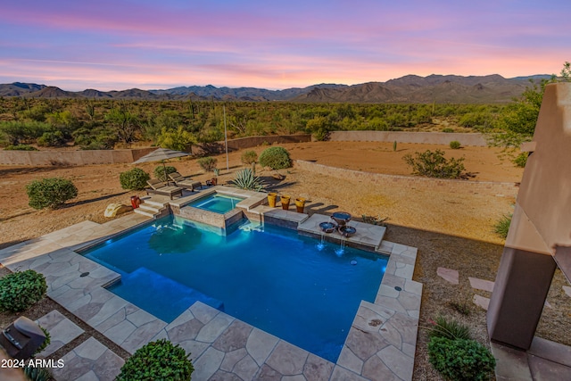 pool at dusk featuring an in ground hot tub, a mountain view, and a patio area