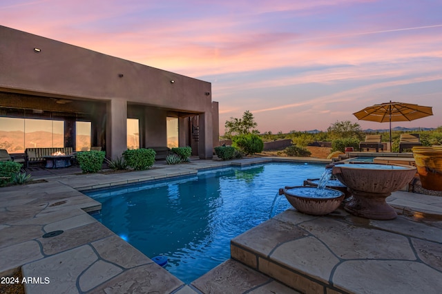 pool at dusk featuring a patio area and a jacuzzi