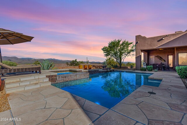 pool at dusk featuring pool water feature, a patio, a mountain view, and an in ground hot tub