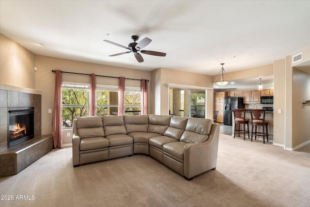 living area with visible vents, baseboards, ceiling fan, a tiled fireplace, and light colored carpet