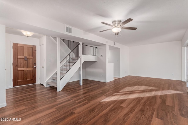 interior space with dark wood-type flooring, visible vents, a ceiling fan, stairs, and baseboards