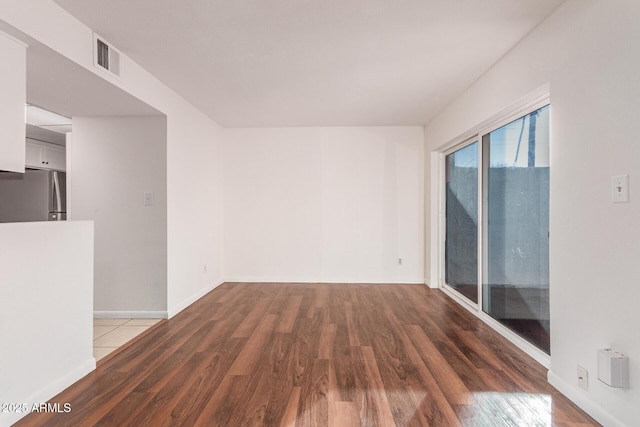 spare room with dark wood-style floors, visible vents, and baseboards