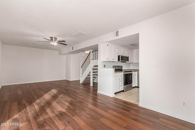 unfurnished living room with light wood-style flooring, visible vents, baseboards, stairs, and a ceiling fan