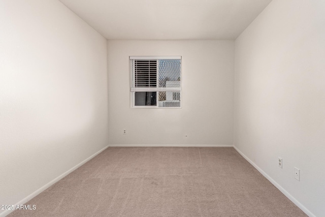 spare room featuring light carpet and baseboards