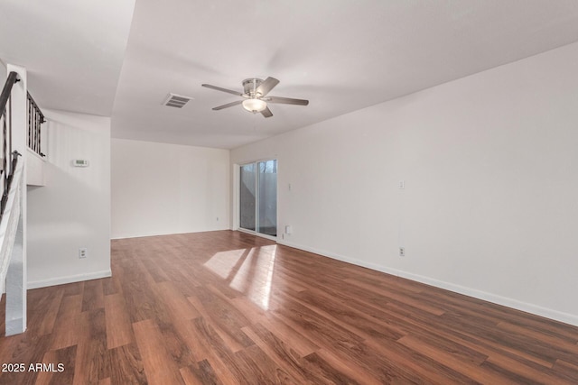 empty room with baseboards, visible vents, a ceiling fan, dark wood-type flooring, and stairs