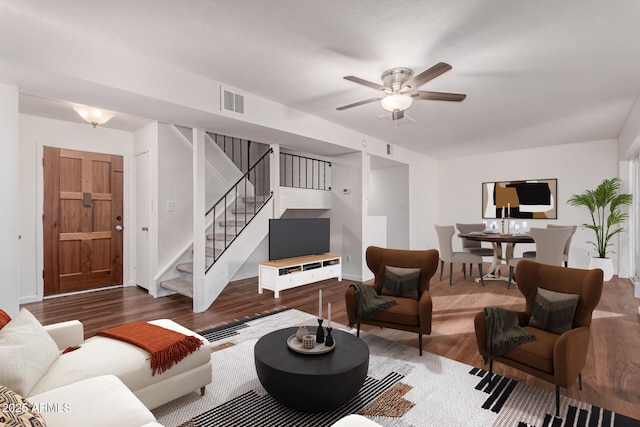 living area featuring ceiling fan, stairs, visible vents, and dark wood-style flooring