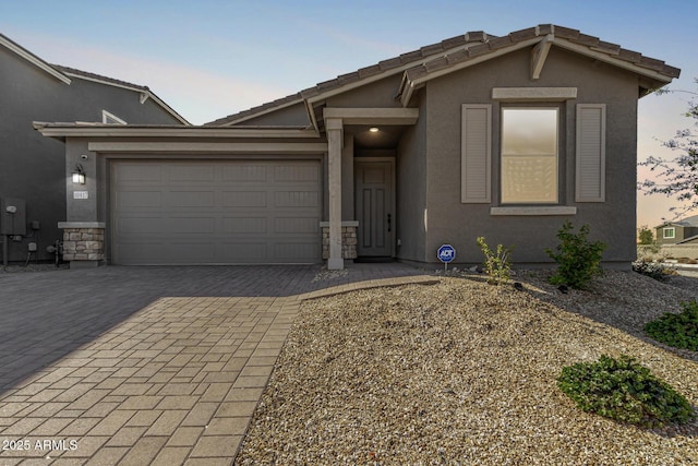 view of front of home featuring stone siding, a garage, decorative driveway, and stucco siding