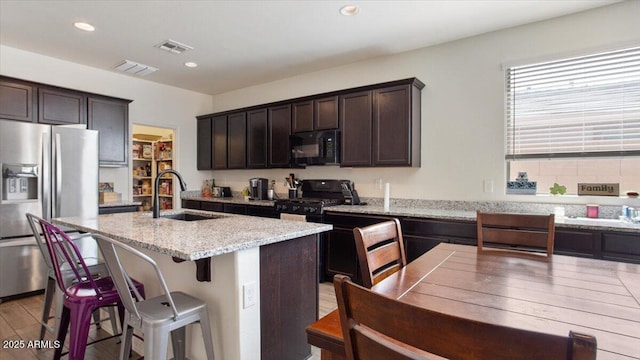 kitchen featuring light stone countertops, light wood finished floors, a sink, black appliances, and dark brown cabinetry
