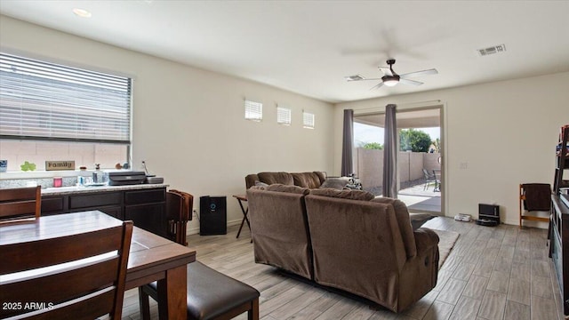 living area featuring visible vents, a ceiling fan, light wood-style floors, and baseboards