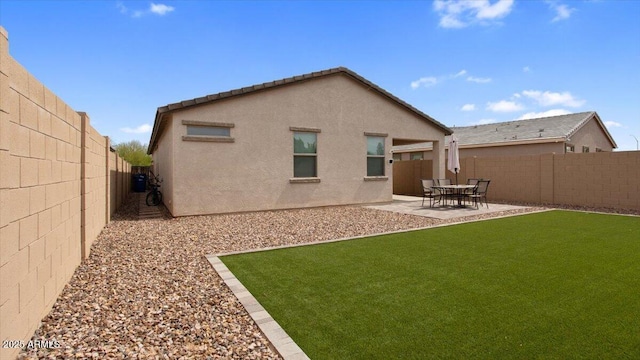 back of house with a fenced backyard, stucco siding, a yard, and a patio