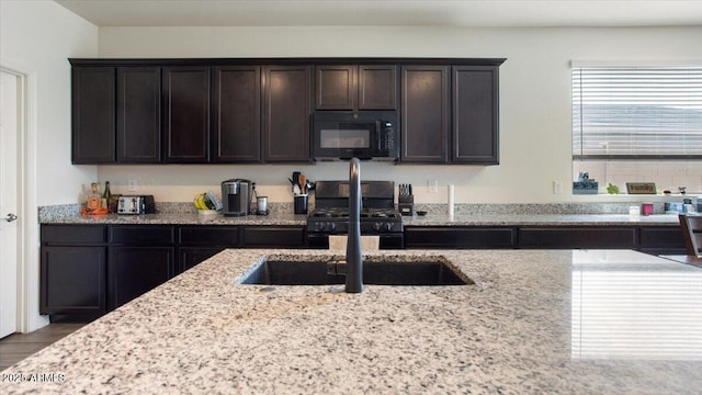 kitchen with dark brown cabinetry, light stone countertops, black appliances, and a sink