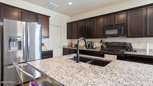 kitchen with dark brown cabinetry, visible vents, black appliances, and a sink