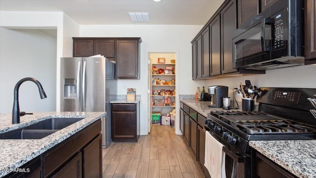 kitchen featuring visible vents, light wood-type flooring, black appliances, a sink, and dark brown cabinetry
