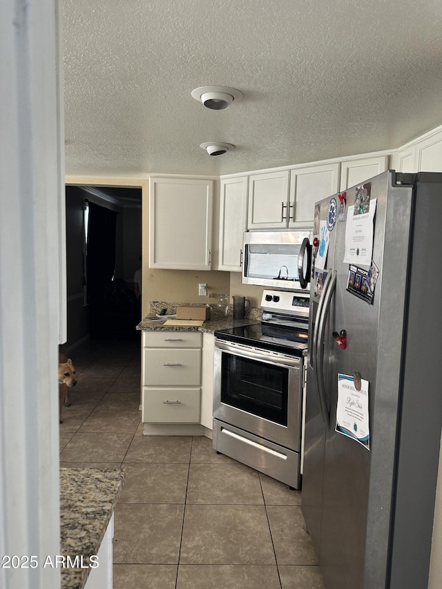 kitchen with white cabinets, stainless steel appliances, dark stone counters, and dark tile patterned flooring