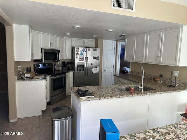 kitchen featuring kitchen peninsula, appliances with stainless steel finishes, sink, white cabinetry, and light tile patterned flooring