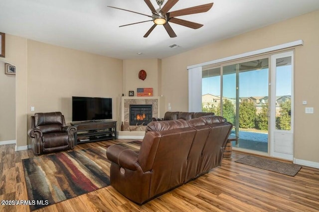 living room with a high end fireplace, ceiling fan, and light wood-type flooring