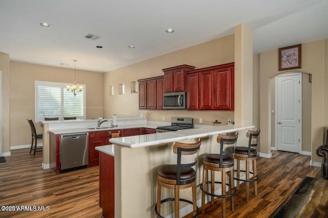 kitchen featuring sink, hanging light fixtures, stainless steel appliances, dark hardwood / wood-style floors, and kitchen peninsula