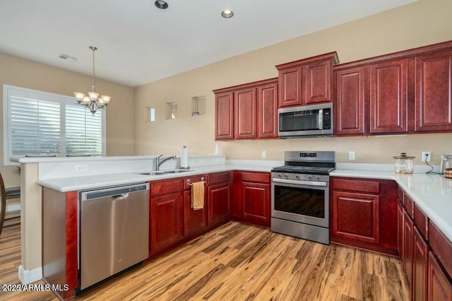 kitchen featuring sink, decorative light fixtures, light hardwood / wood-style flooring, kitchen peninsula, and stainless steel appliances