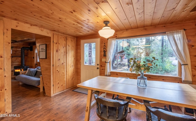 dining room with wooden walls, wooden ceiling, wood finished floors, a wood stove, and a wealth of natural light