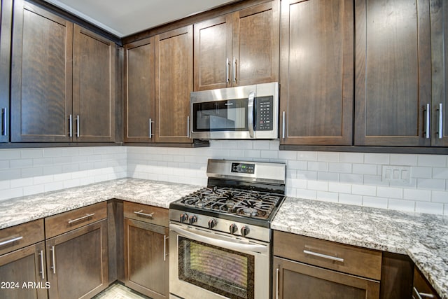 kitchen featuring decorative backsplash, dark brown cabinets, light stone counters, and stainless steel appliances