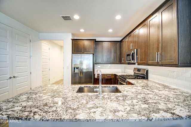 kitchen featuring backsplash, stainless steel appliances, sink, light stone counters, and kitchen peninsula