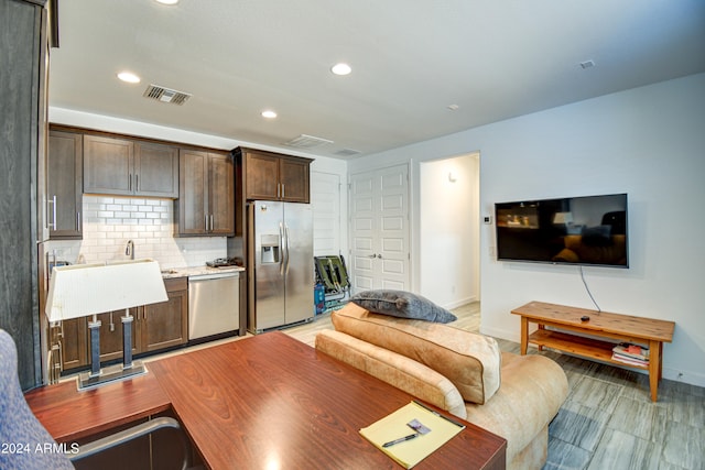 kitchen featuring stainless steel appliances, decorative backsplash, light wood-type flooring, and dark brown cabinetry