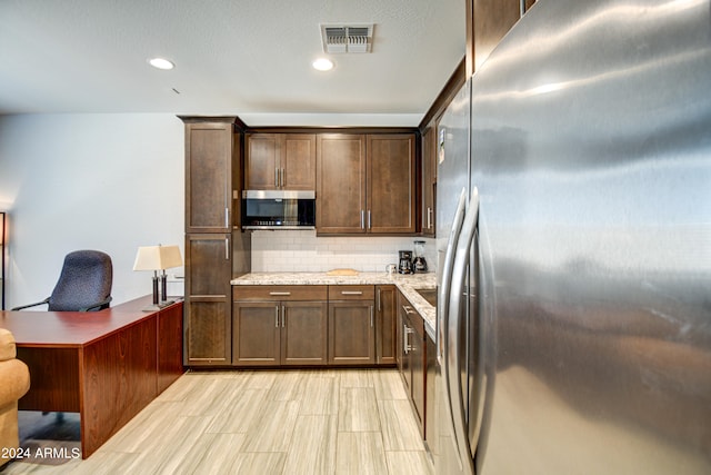 kitchen featuring appliances with stainless steel finishes, light stone counters, dark brown cabinetry, and backsplash