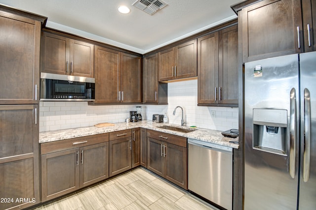 kitchen with sink, decorative backsplash, light stone countertops, and stainless steel appliances