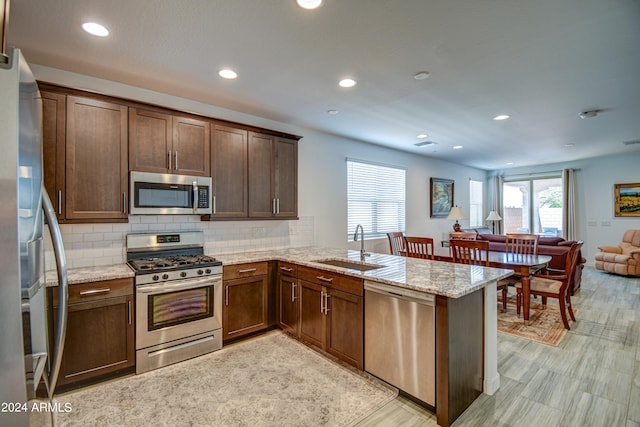 kitchen featuring tasteful backsplash, light stone countertops, sink, kitchen peninsula, and stainless steel appliances