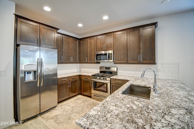 kitchen featuring backsplash, appliances with stainless steel finishes, light stone counters, light tile patterned floors, and sink