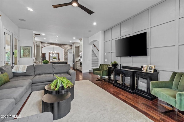 living room featuring stairway, arched walkways, decorative columns, and dark wood-style floors