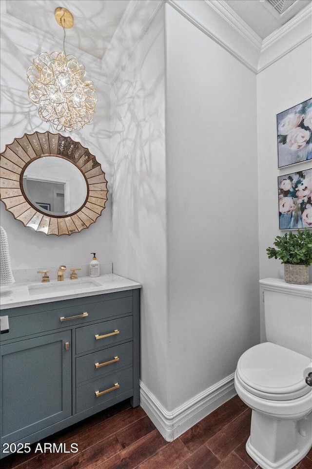 half bath featuring toilet, a chandelier, baseboards, wood finished floors, and ornamental molding