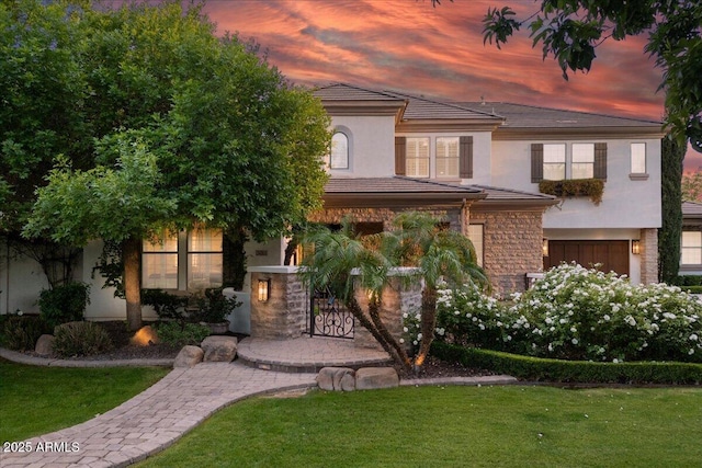 view of front facade with a lawn, a garage, stone siding, and stucco siding