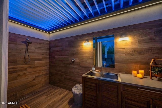 full bathroom featuring tiled shower, vanity, wooden walls, and wood finished floors