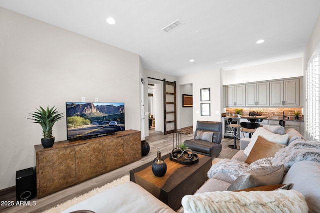 living area featuring a barn door, light wood-style flooring, recessed lighting, and baseboards