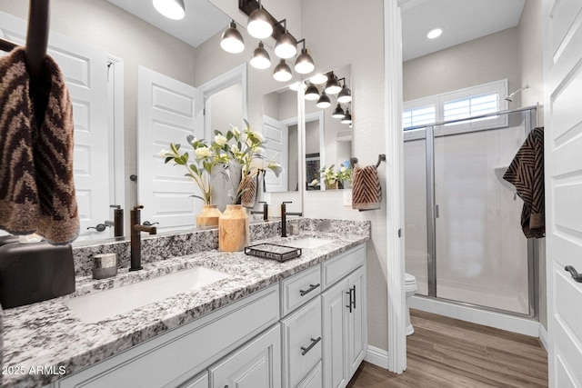 full bathroom featuring a shower stall, double vanity, toilet, wood finished floors, and baseboards