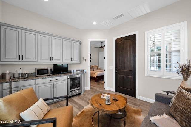 living area featuring beverage cooler, baseboards, light wood-style flooring, and recessed lighting
