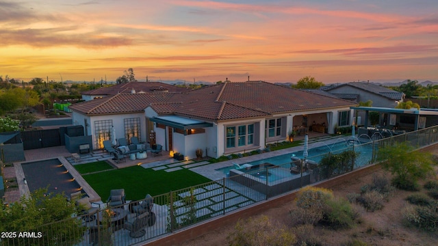 back of house at dusk with a fenced backyard, a tiled roof, an outdoor hangout area, an attached garage, and a patio