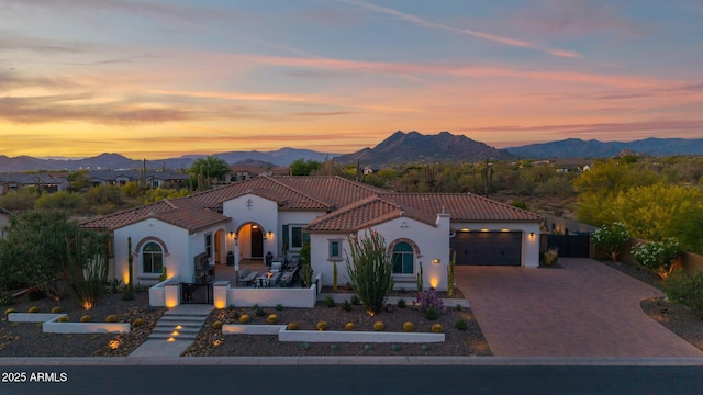 mediterranean / spanish-style home with an attached garage, a tiled roof, a gate, and a mountain view