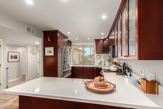 kitchen with kitchen peninsula, stainless steel appliances, sink, and light stone countertops