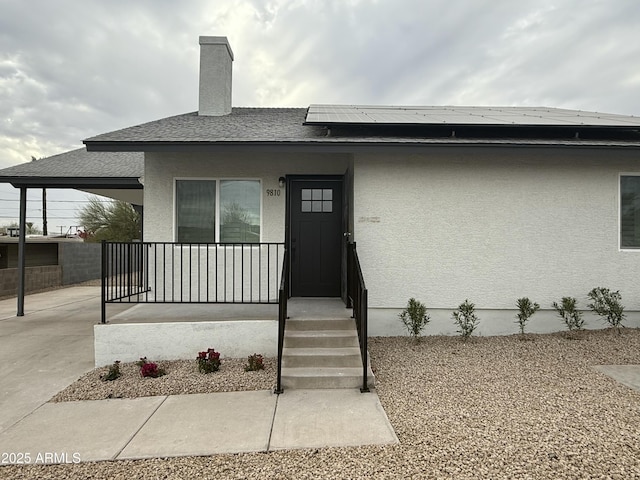 view of front of property featuring roof with shingles, covered porch, a chimney, stucco siding, and roof mounted solar panels