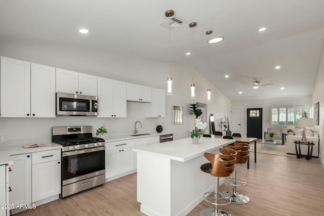 kitchen featuring a sink, open floor plan, a center island, white cabinetry, and appliances with stainless steel finishes