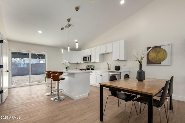 kitchen featuring a breakfast bar, light wood-style flooring, stainless steel appliances, white cabinets, and light countertops