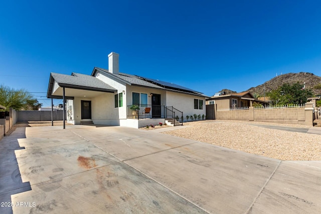 view of front of house featuring roof mounted solar panels, stucco siding, driveway, and fence private yard