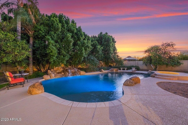 pool at dusk with an in ground hot tub, pool water feature, and a patio