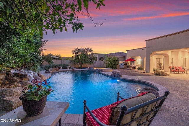 pool at dusk featuring pool water feature, outdoor lounge area, and a patio area