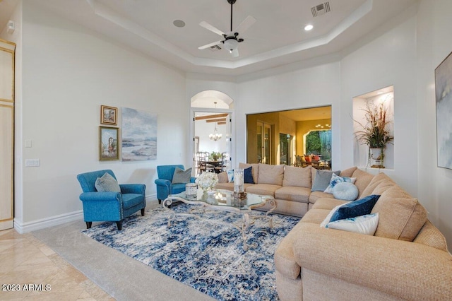 living room featuring a raised ceiling, a towering ceiling, and ceiling fan with notable chandelier