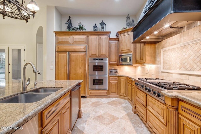 kitchen with sink, custom exhaust hood, light stone counters, built in appliances, and hanging light fixtures